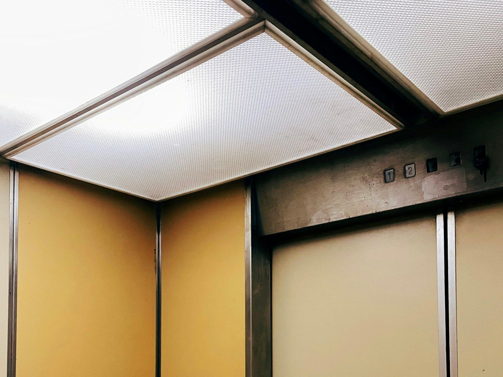 Intérieur de cabine d’ascenseur : parois ocre, portes et plafond lumineux